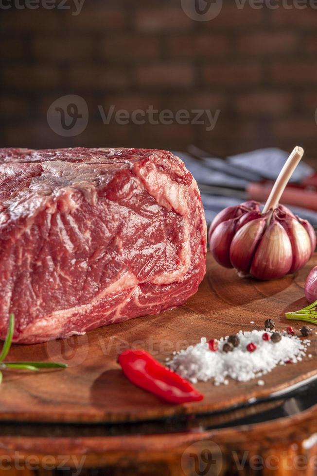 rauwe entrecote rundvlees op een houten snijplank met kruiden op bakstenen muur achtergrond - close-up. foto