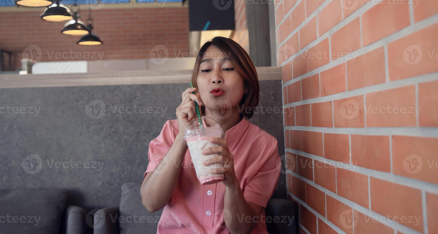 vrouw zittend Aan sofa in de koffie winkel Holding glad sap in plastic en drinken glad gezond aan het eten fruit met grappig gezicht, genieten levensstijl concepten, geluk vakantie. foto