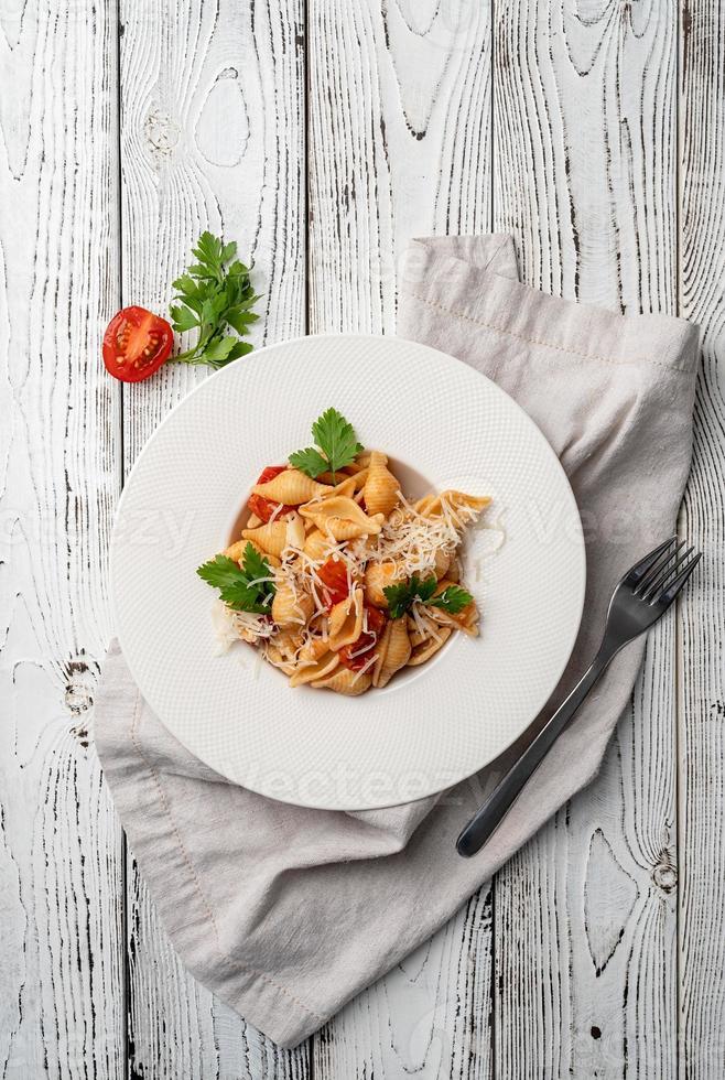 conchiglioni pasta met bolognese saus met kerstomaatjes, kaas en peterselie in witte plaat op houten achtergrond foto