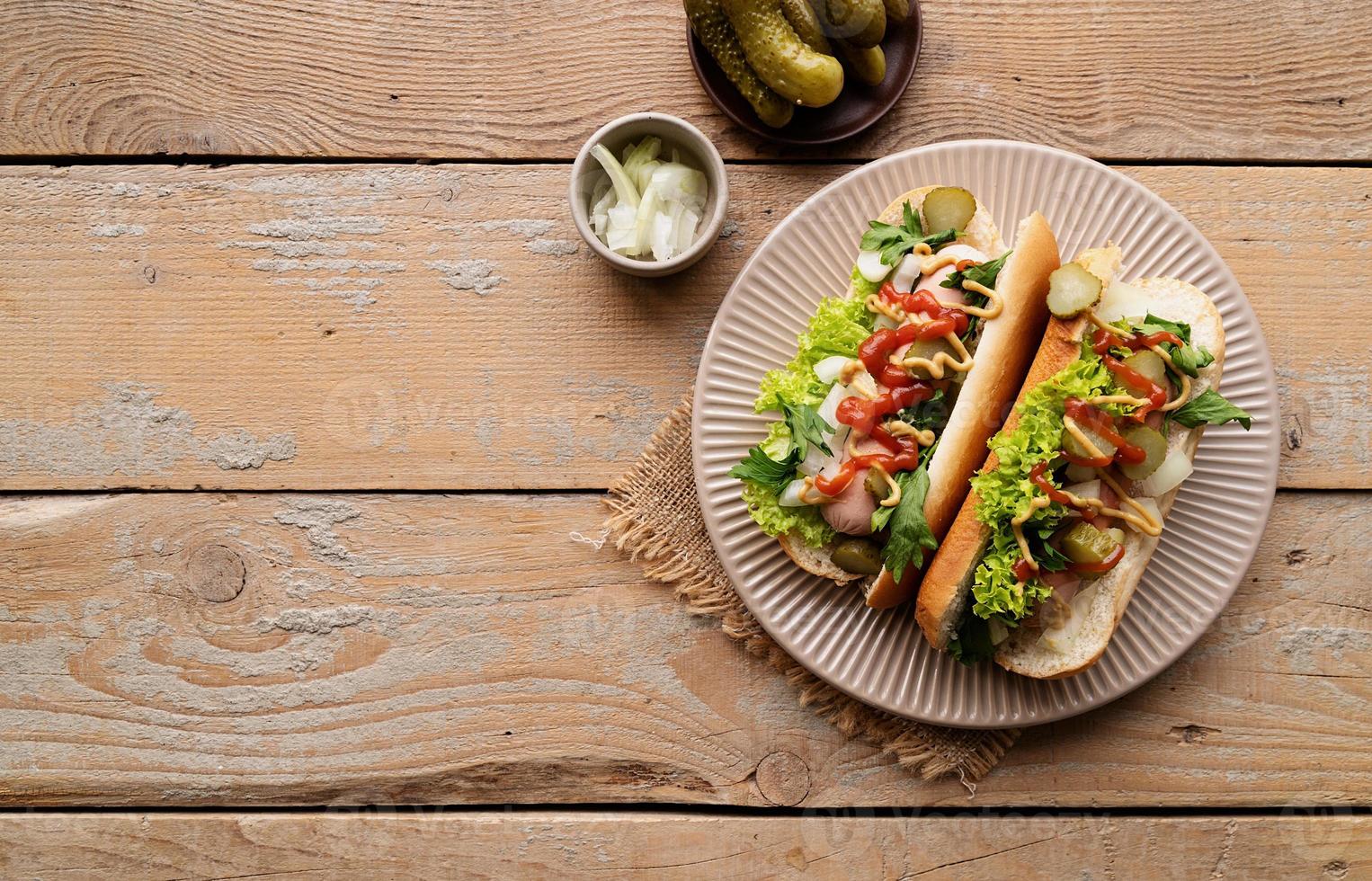 hotdog met worst, sla, komkommer en ui op beige plaat op houten achtergrond foto