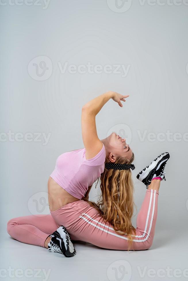 acrobaatvrouw die roze sportkleding draagt die in de studio uitwerkt die op grijze achtergrond wordt geïsoleerd foto