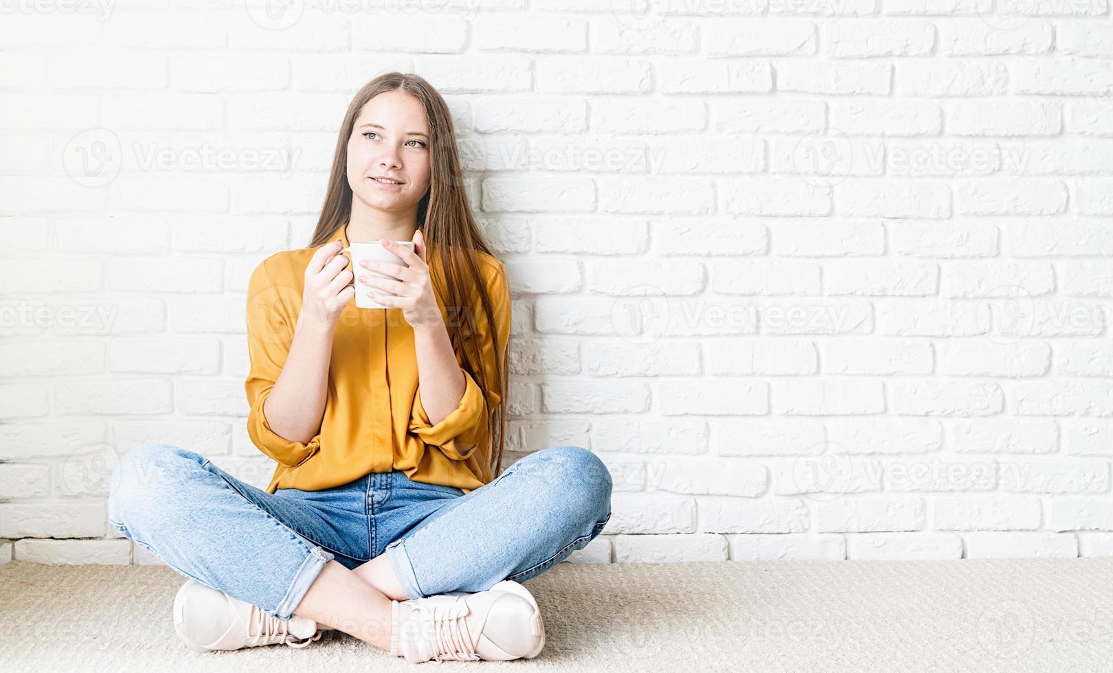 aantrekkelijke tienervrouw in geel overhemd die thee drinkt zittend op de vloer foto