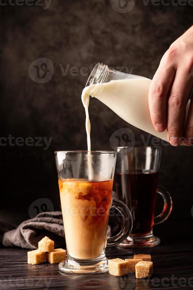 mannenhand gieten melk in hete zwarte thee vooraanzicht op donkere achtergrond foto