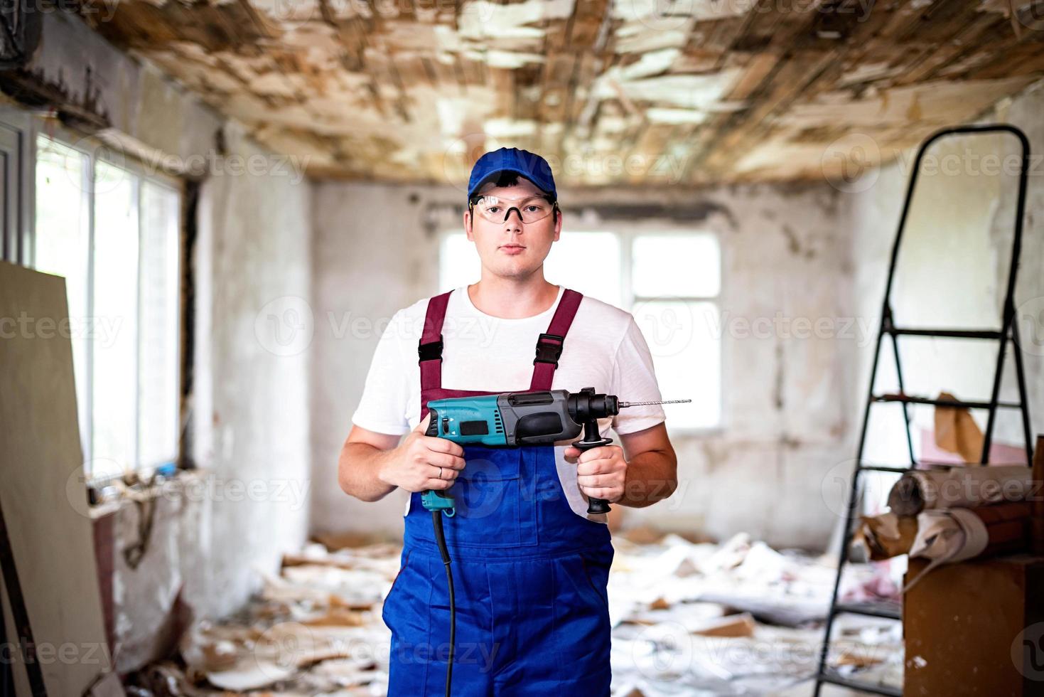 bouwvakker in beschermingsbril en uniform met perforator. man met boor foto