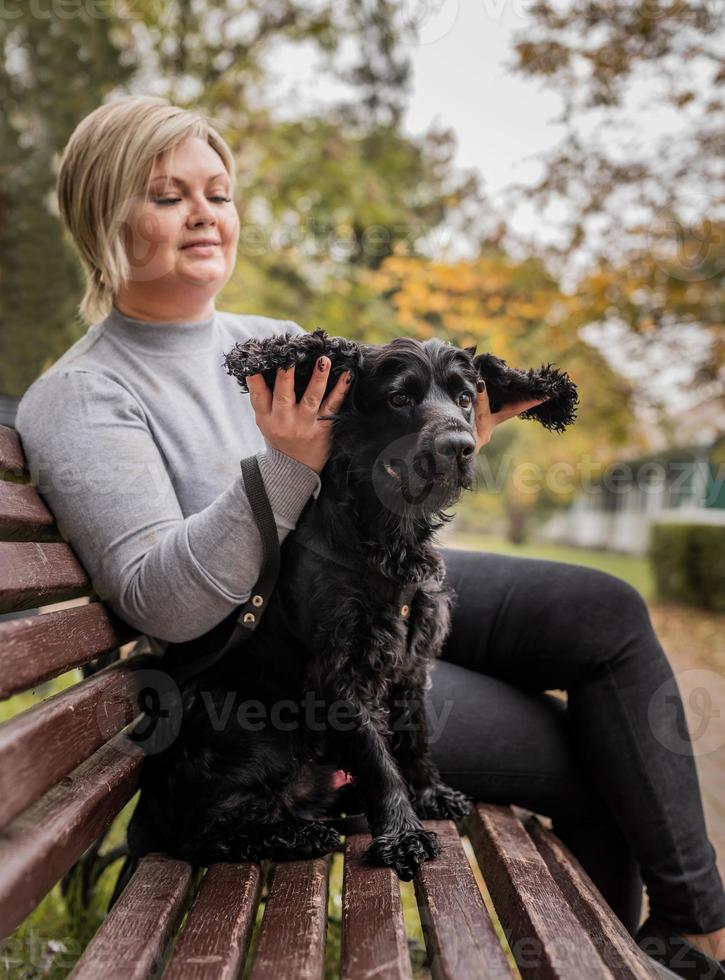 jonge vrouw die haar cocker-spaniëlhond knuffelt op de bank in het park foto