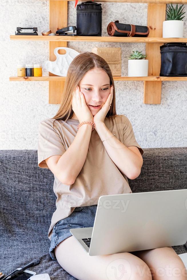 geschokt tienermeisje dat thuis haar laptop studeert foto