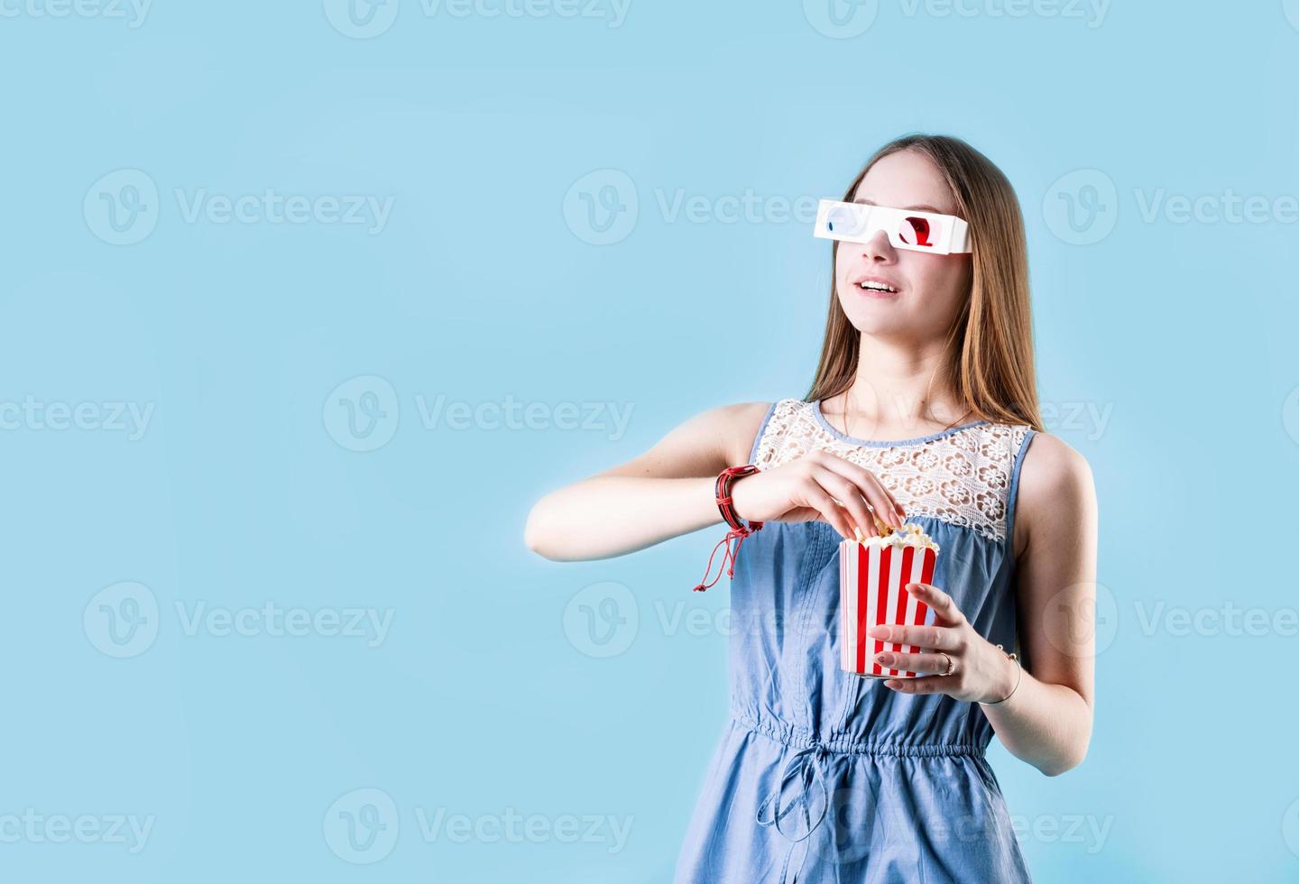 opgewonden vrouwelijk tienermeisje met een 3d-bril die popcorn eet die op een blauwe achtergrond wordt geïsoleerd foto