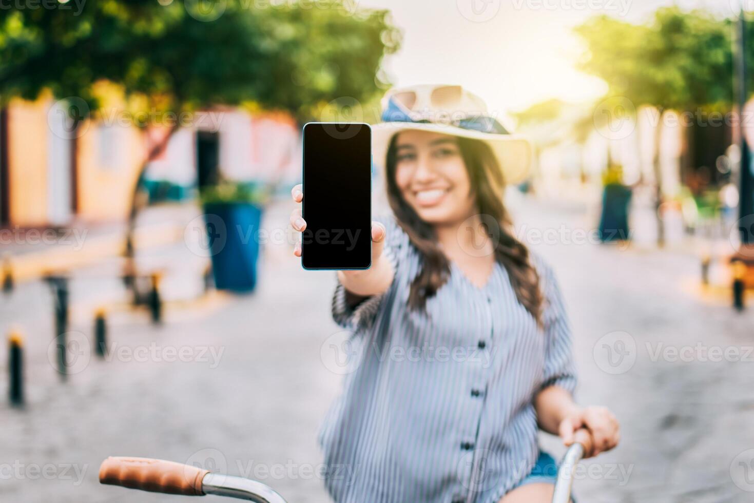 glimlachen toerist Aan fiets tonen cel telefoon scherm Aan de straat. mooi meisje met hoed Aan fiets tonen cel telefoon scherm Aan de straat foto