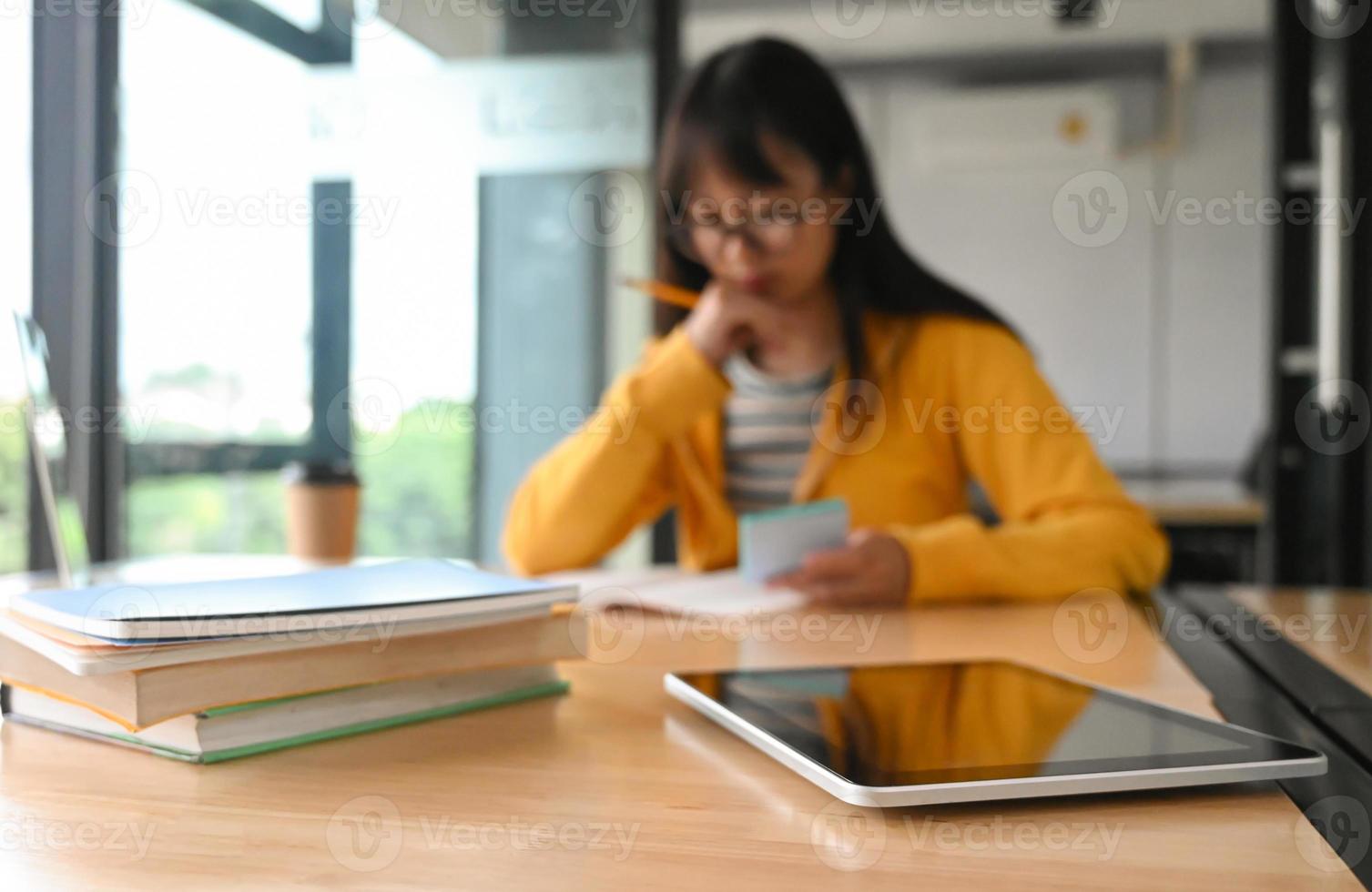 tablet en veel boeken op tafel. achter de student die een boek leest. foto