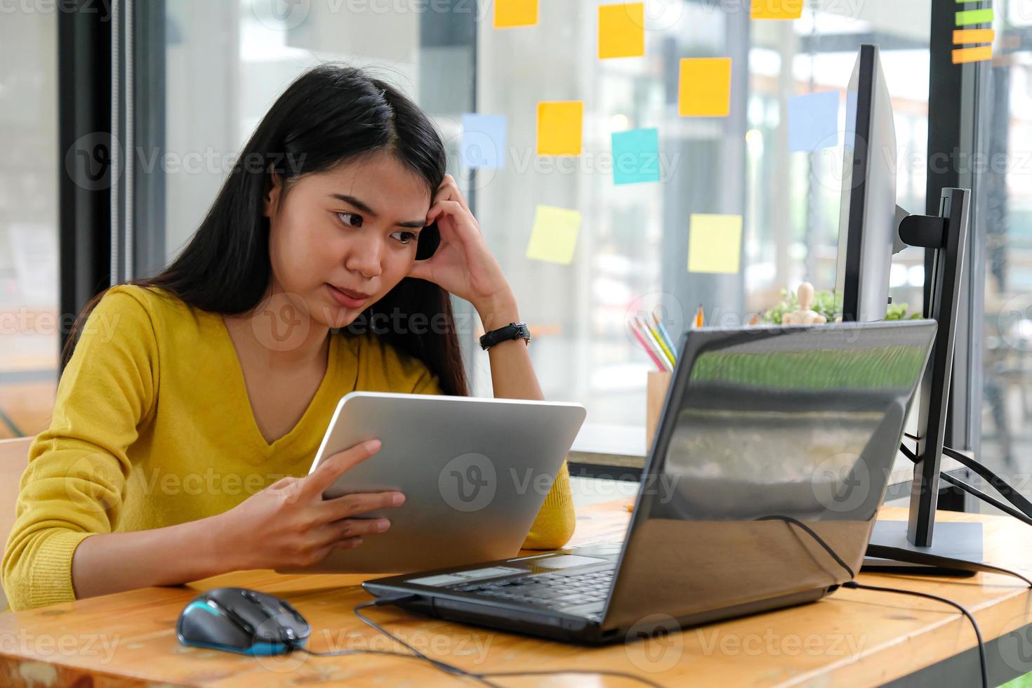 aziatische vrouwelijke programmeur draagt gele shirts, kijkt naar het laptopscherm en houdt een tablet vast. ze toonde een serieuze manier. foto