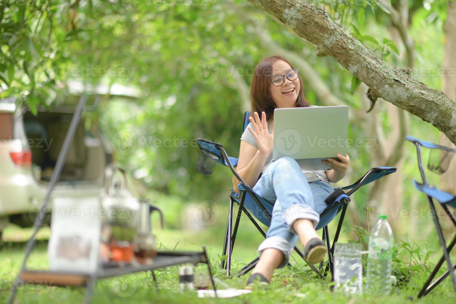 vrouw chatten met vrienden met een laptop tijdens het kamperen. foto