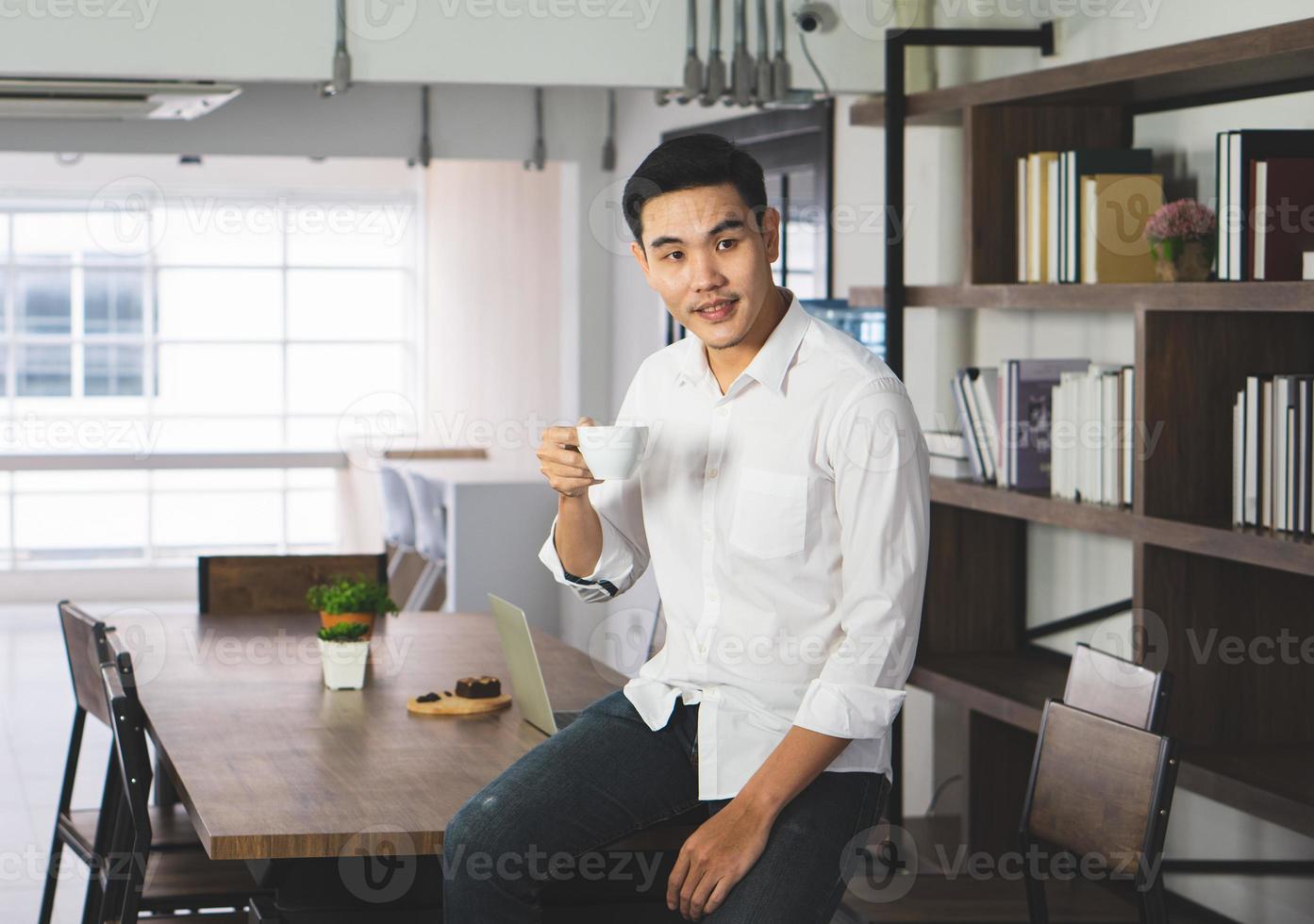 aziatische man zit in het café, drinkt koffie en ontbijt, wakker van de afstand. bedrijfs- en technologieconcept foto