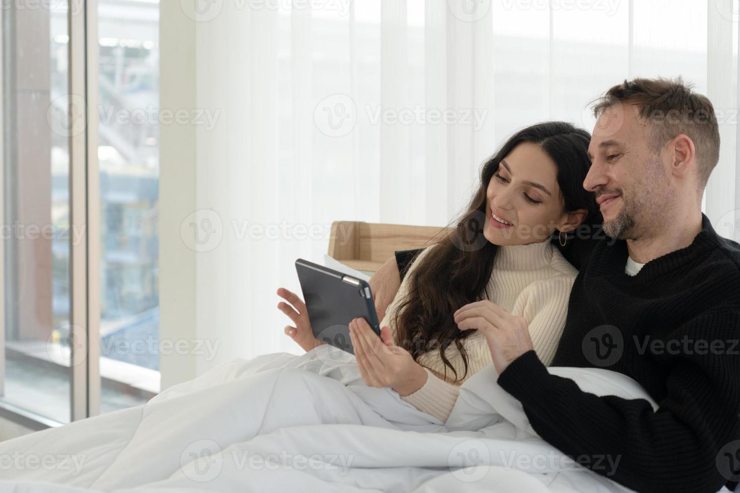 Kaukasisch paar zittend in bed en films kijken vanaf tablet in slaapkamer thuis. saamhorigheid concept foto