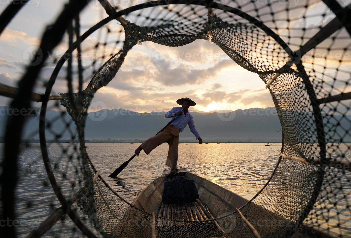 kijk door het vishok van een lokale visser die bij zonsopgang op de boot in het meer staat foto
