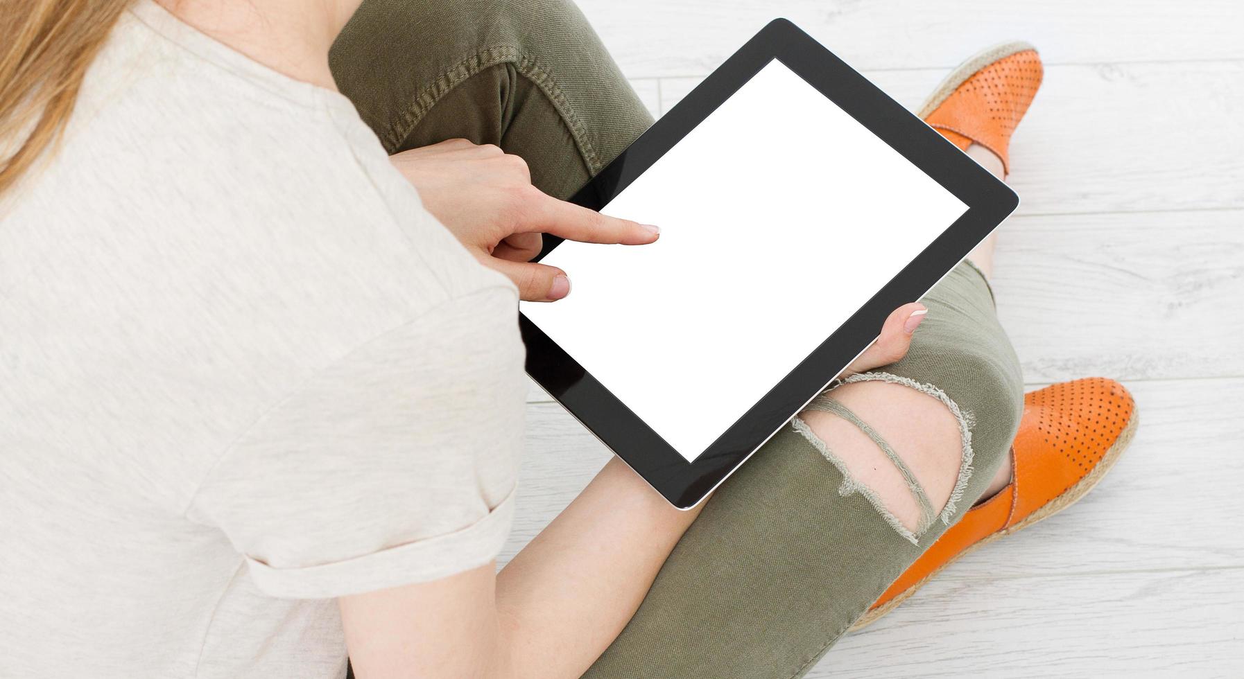 tiener vrouw meisje met behulp van een tablet pc zittend op de vloer in een woonkamer, leeg scherm aan te raken foto