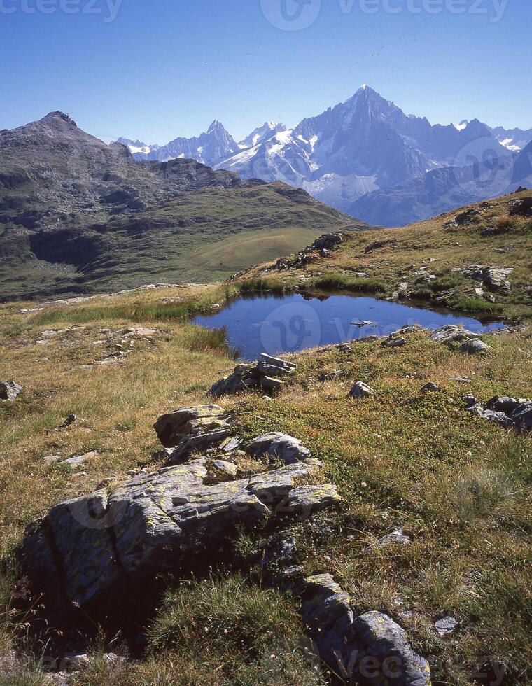 een klein vijver in een met gras begroeid veld- met bergen in de achtergrond foto