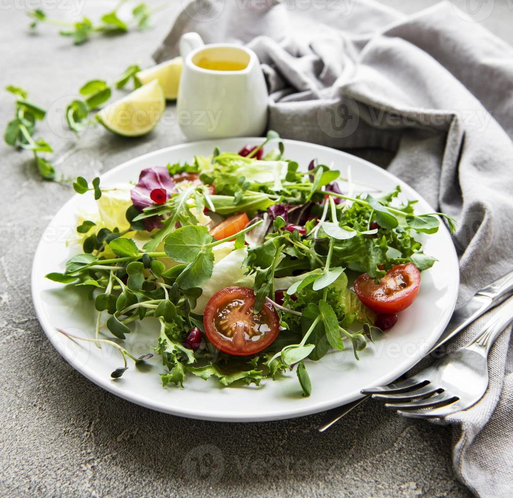 verse groene gemengde slakom met tomaten en microgreens op betonnen ondergrond. gezonde voeding, bovenaanzicht. foto