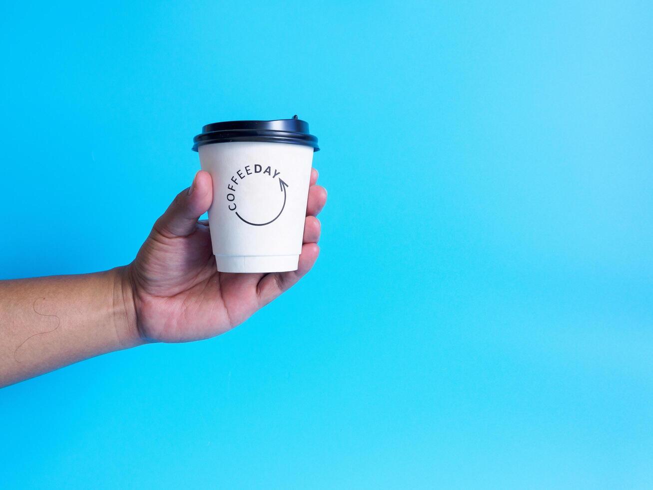 Mens hand- Holding een wit koffie kop gevulde met heet zwart koffie americano Nee suiker Nee melk, klaar naar drankje, verfrissend. aroma wakker vers naar werk geplaatst Aan een blauw geïsoleerd achtergrond foto