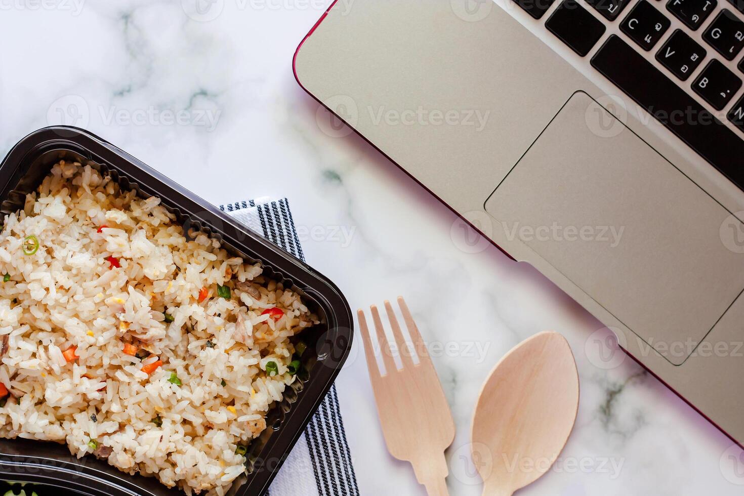 heerlijk gebakken rijst- in lunch doos Aan tafellinnen met houten lepel en vork en computer laptop Bij werkplaats foto