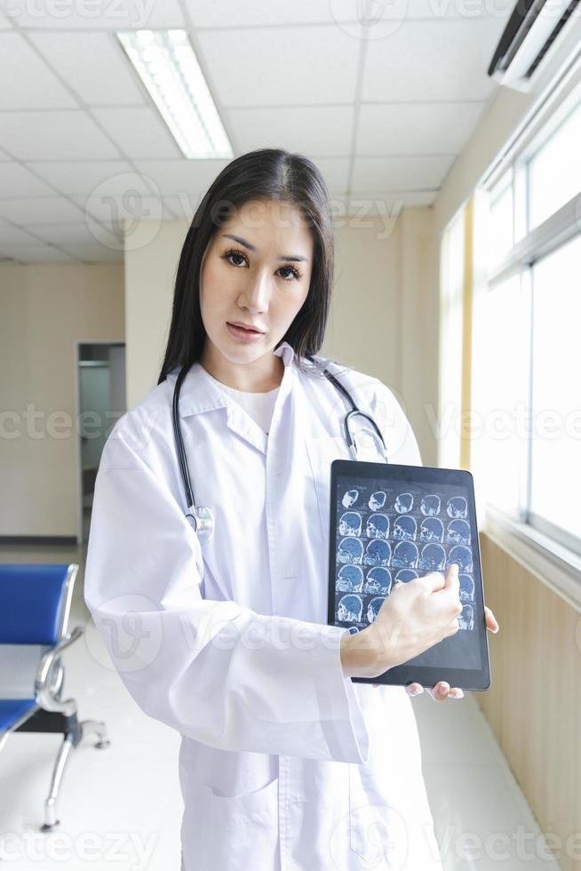 portret van slimme vrouwelijke arts die tablet vasthoudt om röntgenfoto's te tonen en bij de receptie van het ziekenhuis staat. foto