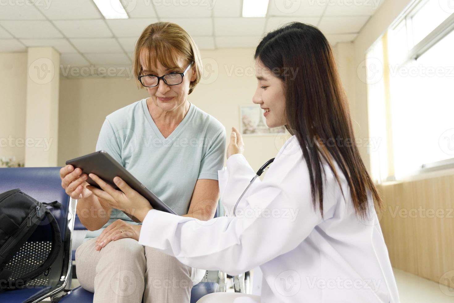 vrouwelijke arts geeft advies aan de oude vrouw patiënt via een tablet in het ziekenhuis. foto