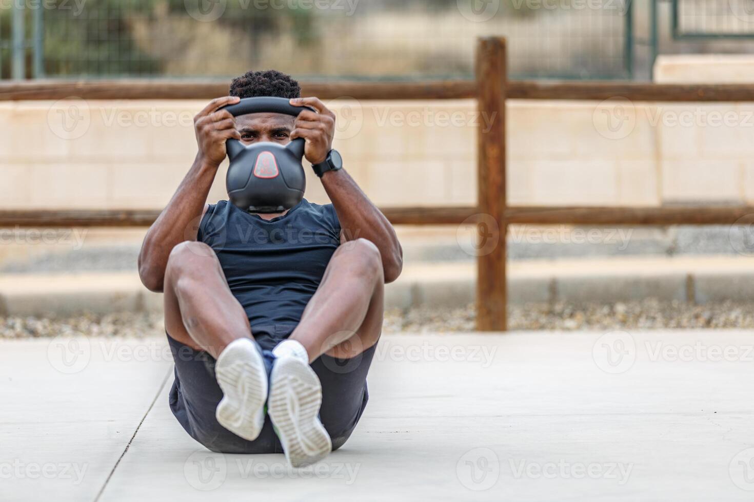 zwart Mens in activewear aan het doen buikspieren training met kettlebell gedurende buitenshuis oefening foto