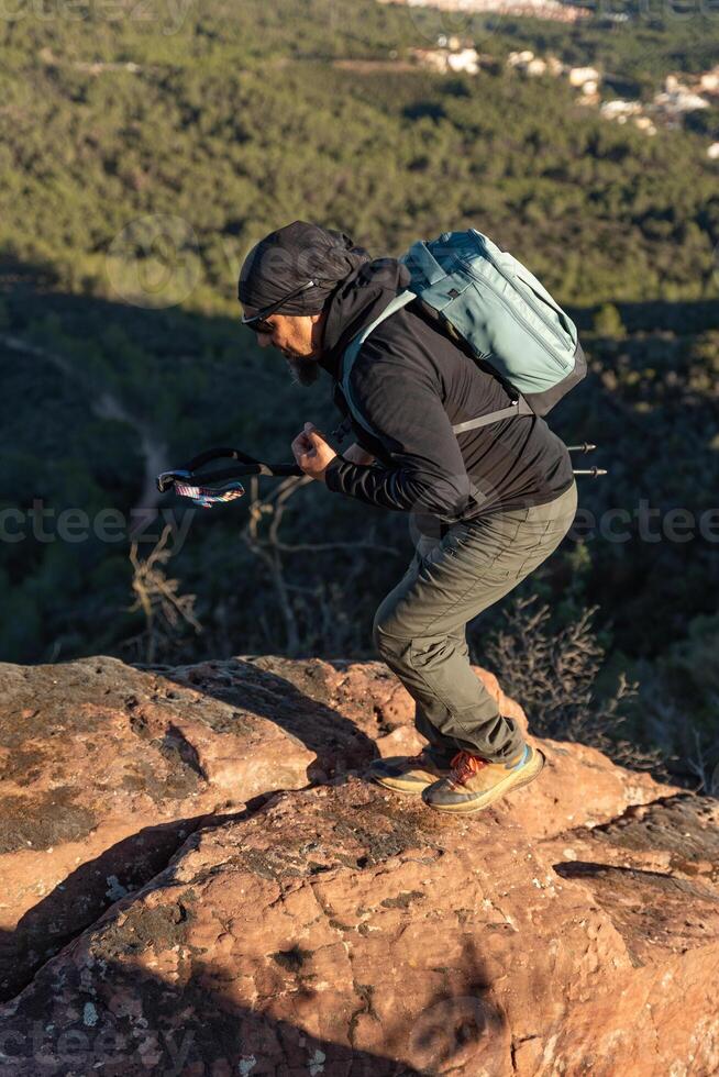 middelbare leeftijd Mens klimt de berg in de garraf natuurlijk park, ondersteund door wandelen palen. foto