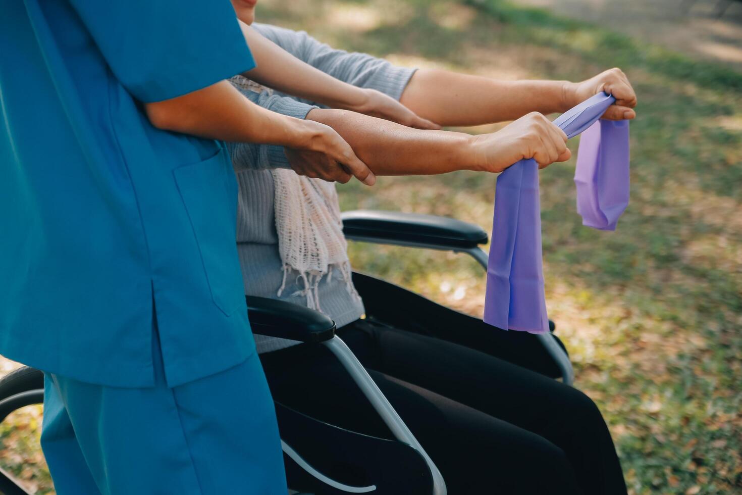 jong verpleegster of fysiotherapeut in scrubs helpen een gelukkig gepensioneerd oud vrouw Doen geschiktheid opdrachten met licht gewicht halters Bij huis. concept van fysiotherapie voor senioren foto