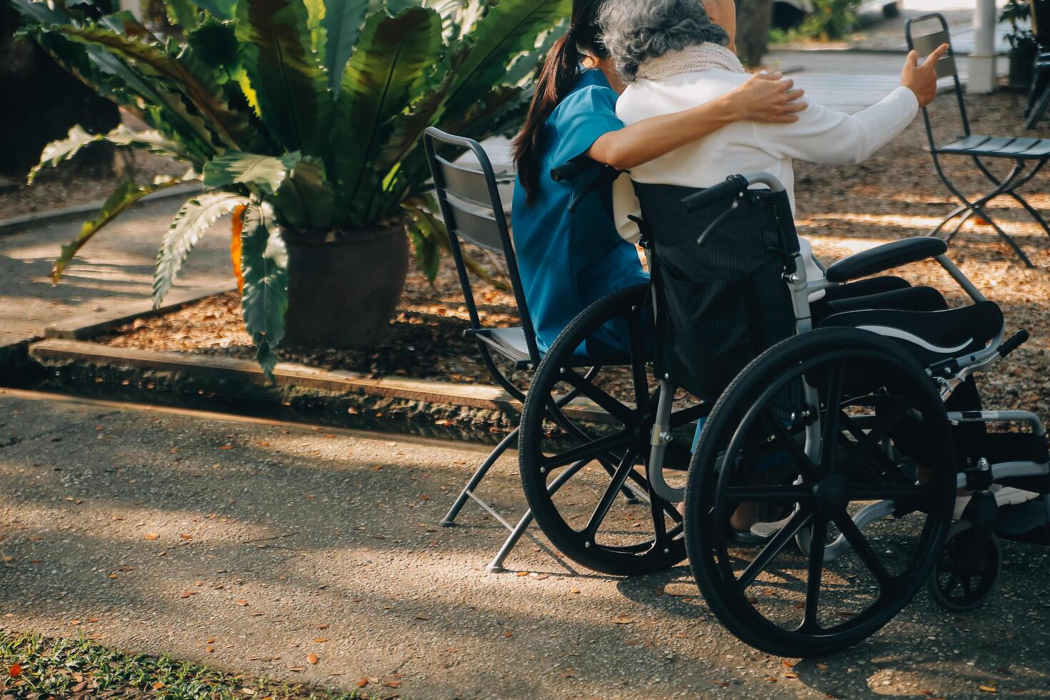 een verpleegster nemen zorg een senior mannetje Aan rolstoel in zijn tuin Bij huis foto