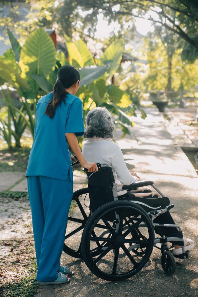 een verpleegster nemen zorg een senior mannetje Aan rolstoel in zijn tuin Bij huis foto