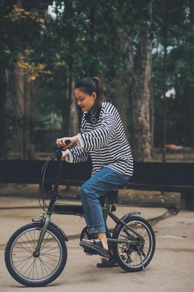 gelukkig Aziatisch jong vrouw wandelen en rijden fiets in park, straat stad haar glimlachen gebruik makend van fiets van vervoer, eco vriendelijk, mensen levensstijl concept. foto