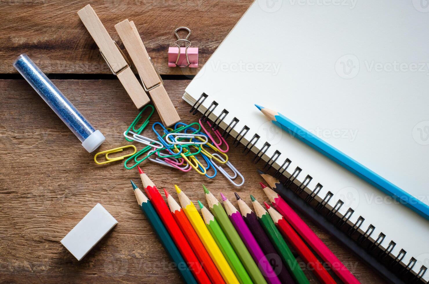 kleurpotloden, gummen, notitieboekje, klem Aan een houten vloer. foto