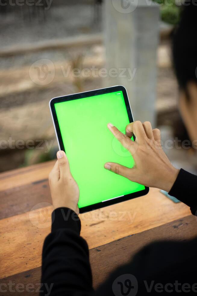 bespotten omhoog foto van een dichtbij omhoog schot met een mans hand- Holding een ipad tablet met een groen scherm tegen de achtergrond van een hout cafe tafel