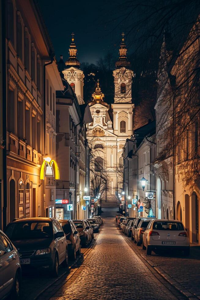 ai gegenereerd beeld van prachtig verlichte barok stijl kerk, genesteld tussen klassiek bouwkundig gebouwen Aan geplaveide straat Bij nacht ai gegenereerd foto
