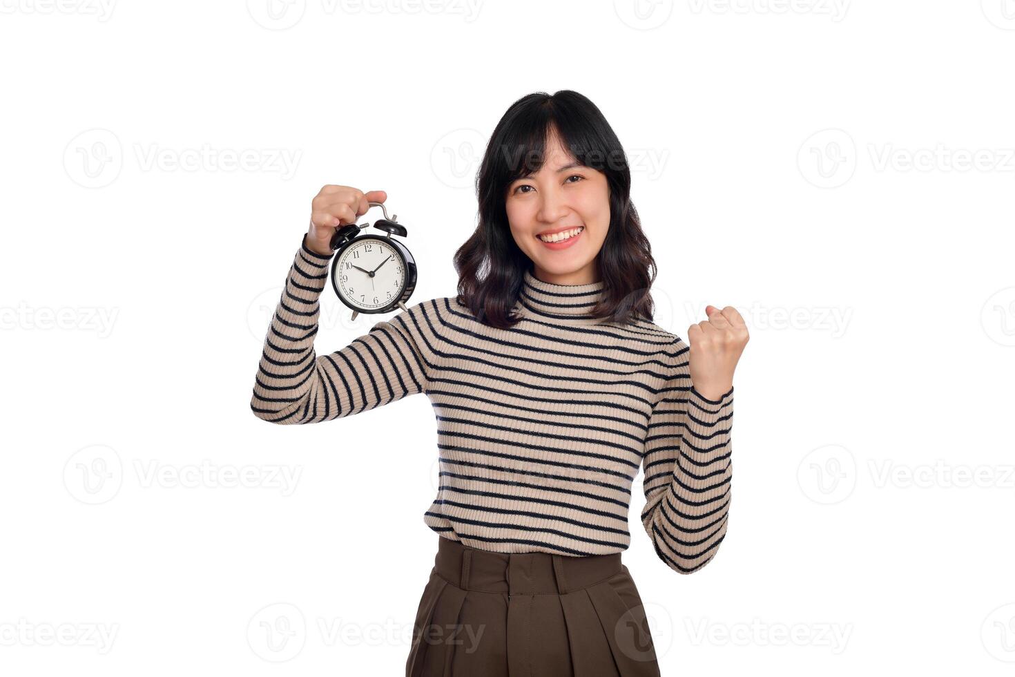 glimlachen vrolijk aantrekkelijk jong Aziatisch vrouw vervelend trui overhemd Holding alarm klok tonen vuist omhoog op zoek camera geïsoleerd Aan wit achtergrond, studio portret foto