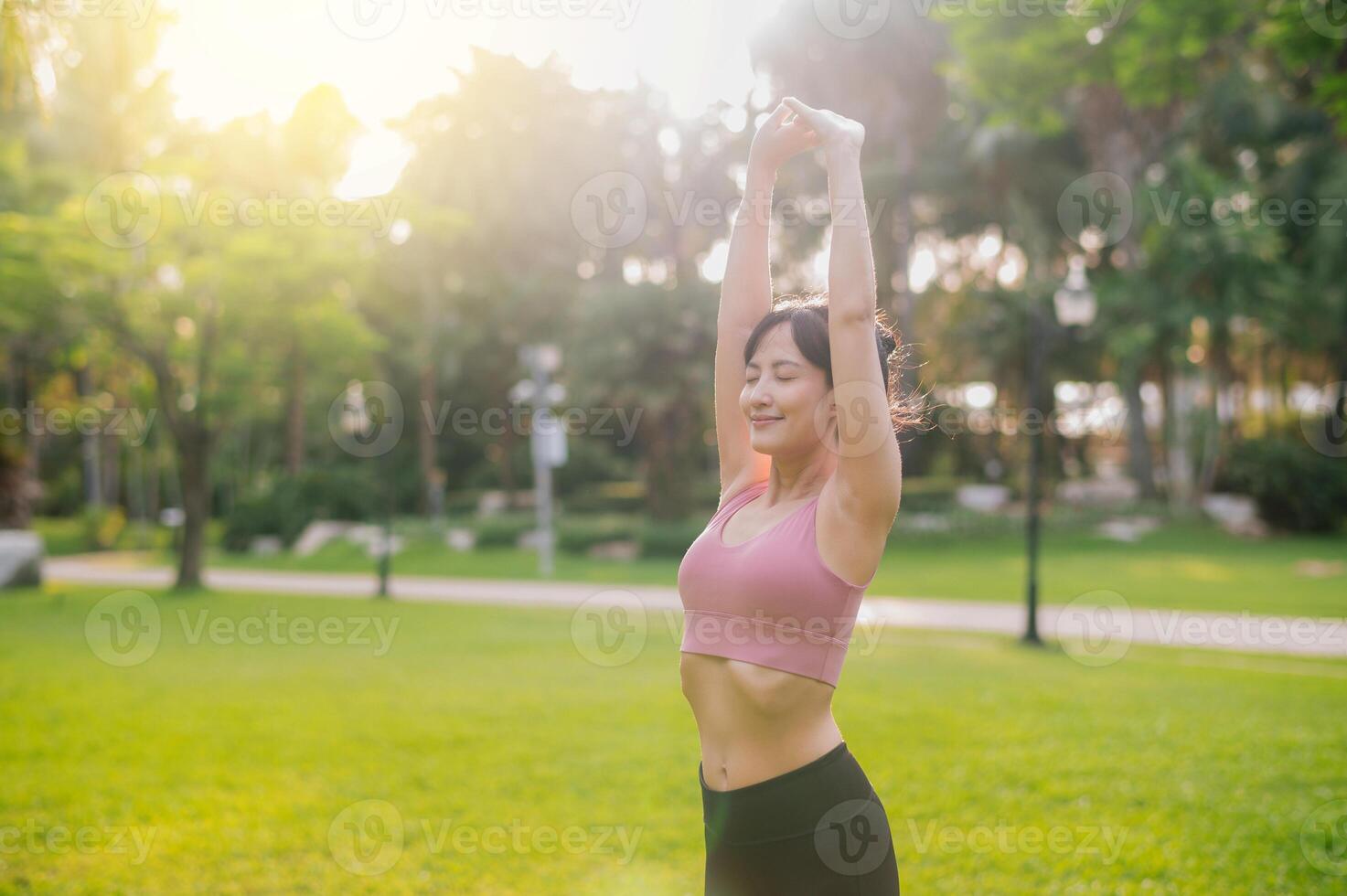 ervaring de vreugde van een Vrolijk, fit vrouw jogger in haar jaren '30 Aziatisch vrouw vervelend roze sportkleding, genieten van vers lucht in een openbaar park. omhelzing welzijn leven en aansluiten met natuur. foto