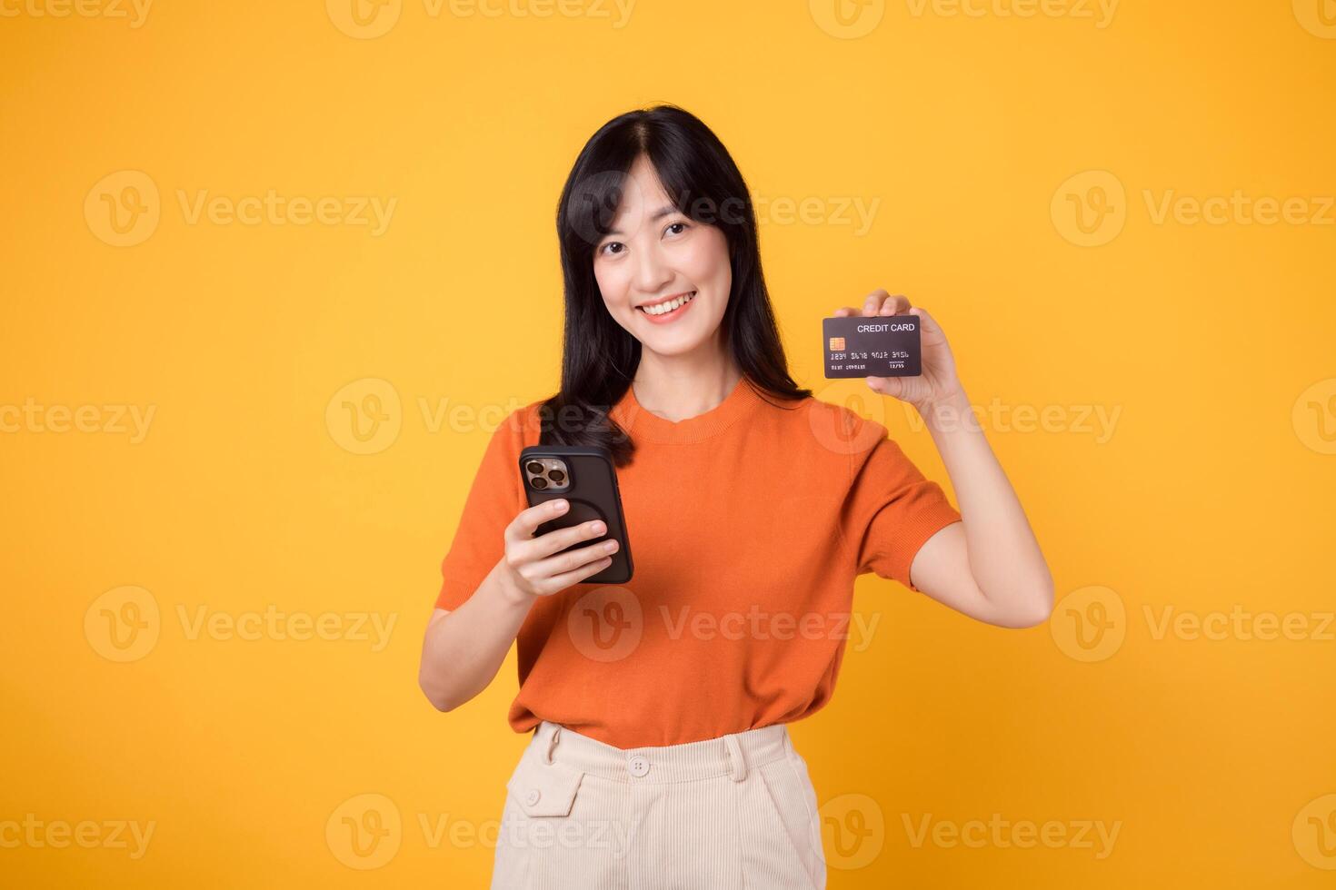 energiek Aziatisch vrouw in haar jaren '30, gebruik makend van smartphone en tonen credit kaart Aan geel achtergrond. snel online winkelen. foto