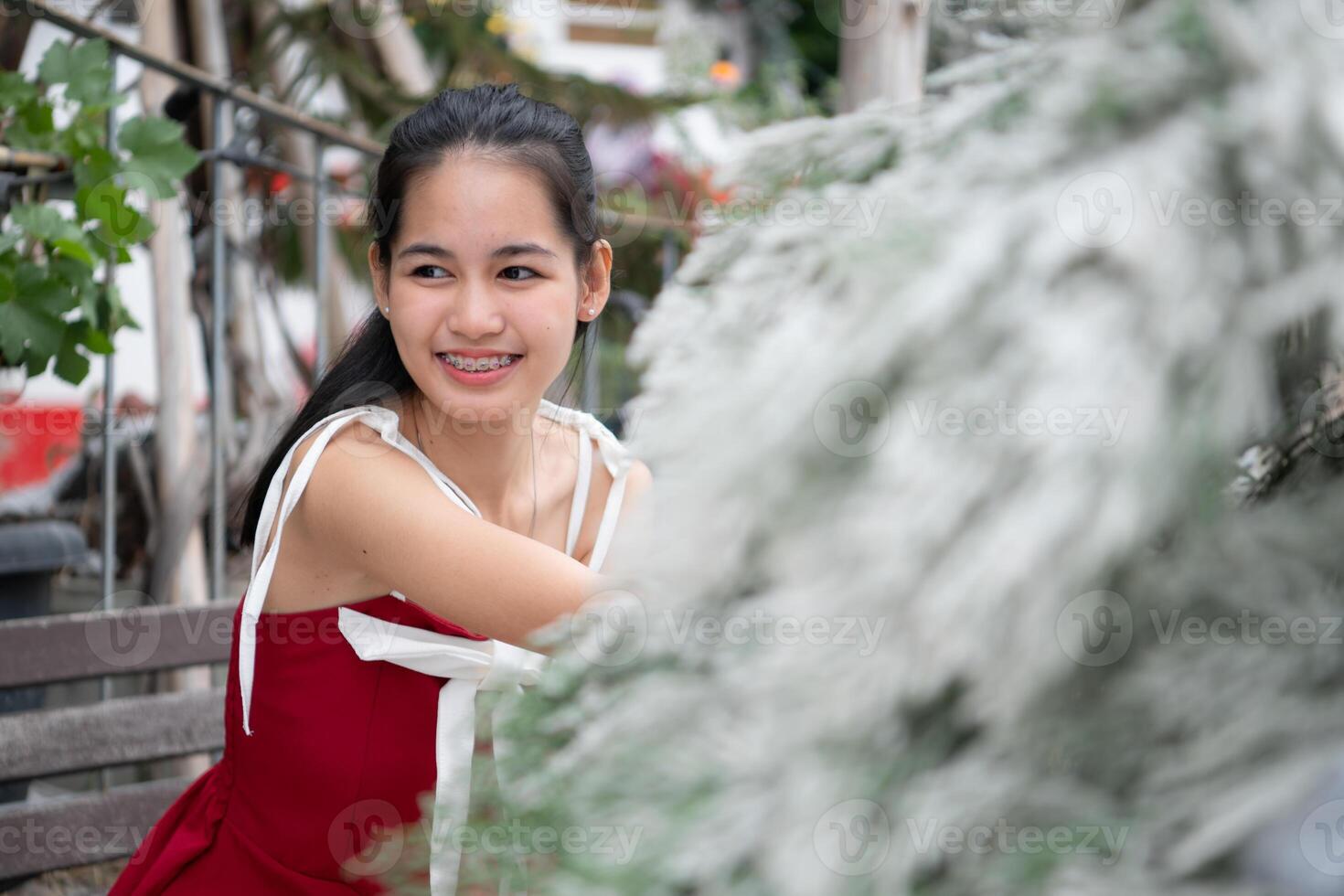 portret van tiener- meisje in een rood jurk ontspannen en glimlachen in een besneeuwd tuin. foto