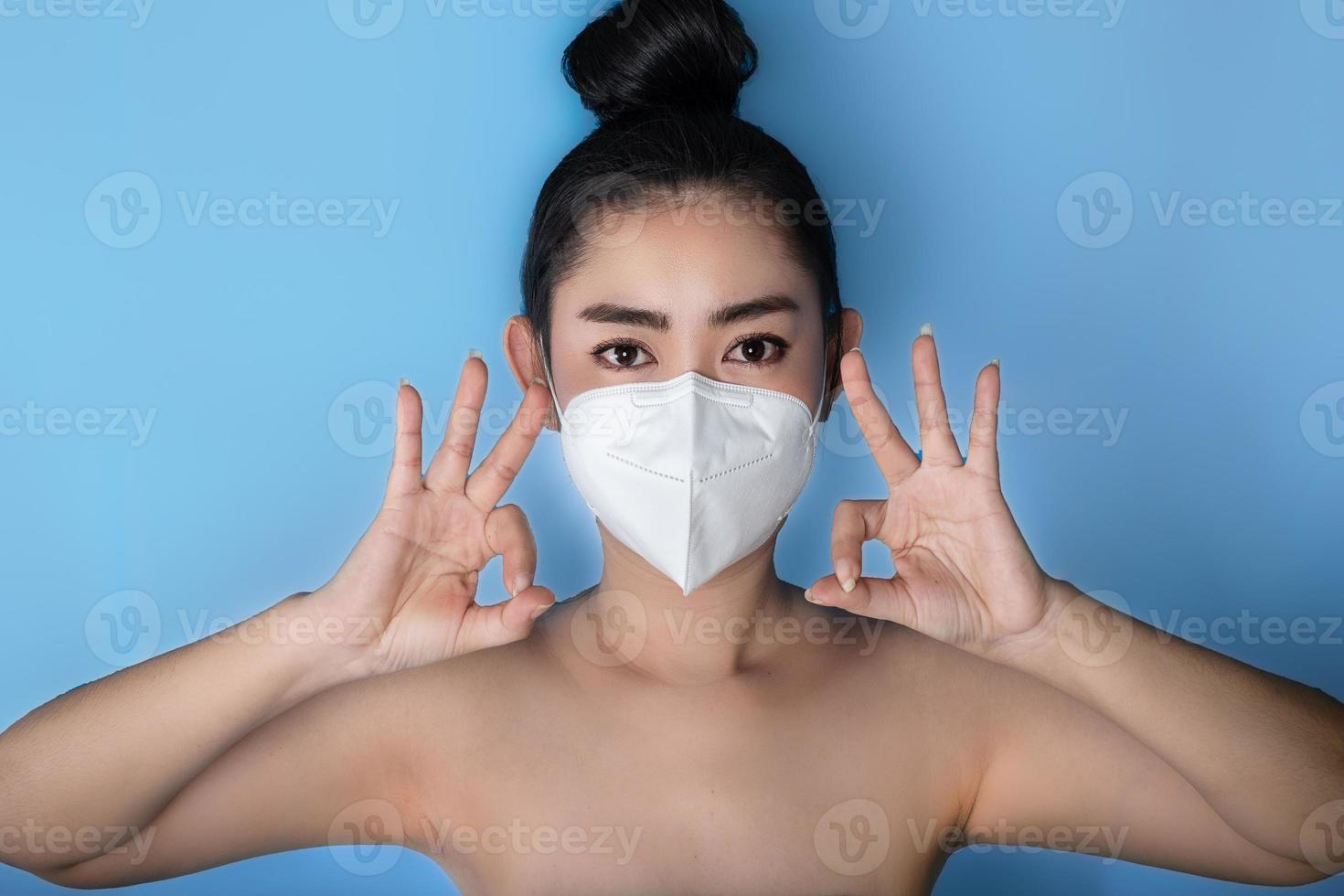 close-up van een vrouw die een respirator n95-masker opzet ter bescherming tegen luchtwegaandoeningen als griep covid-19 corona pm2.5 stof en smog, vrouwelijk duim omhoog gebaar met hand die ok teken toont foto