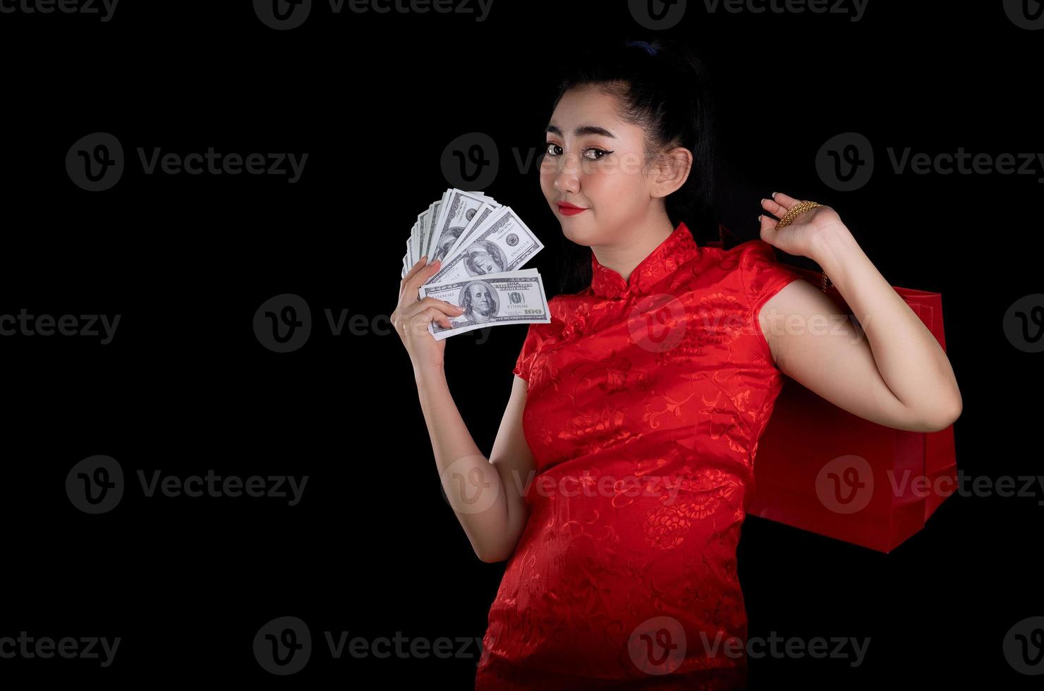 portret van een mooie jonge azië vrouw rode jurk traditionele cheongsam met een tas winkelen en geld bankbiljet 100 usd op de zwarte achtergrond foto