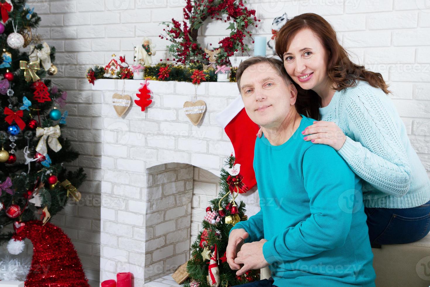 echtpaar van middelbare leeftijd in de kerstkamer, nieuwjaarsopen haard en kerstboom, liefhebbende familie foto