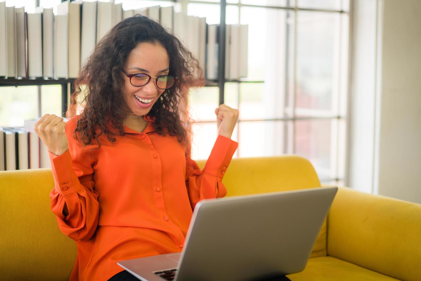 Latijnse vrouw die met laptop op bank met gelukkig gevoel werkt foto