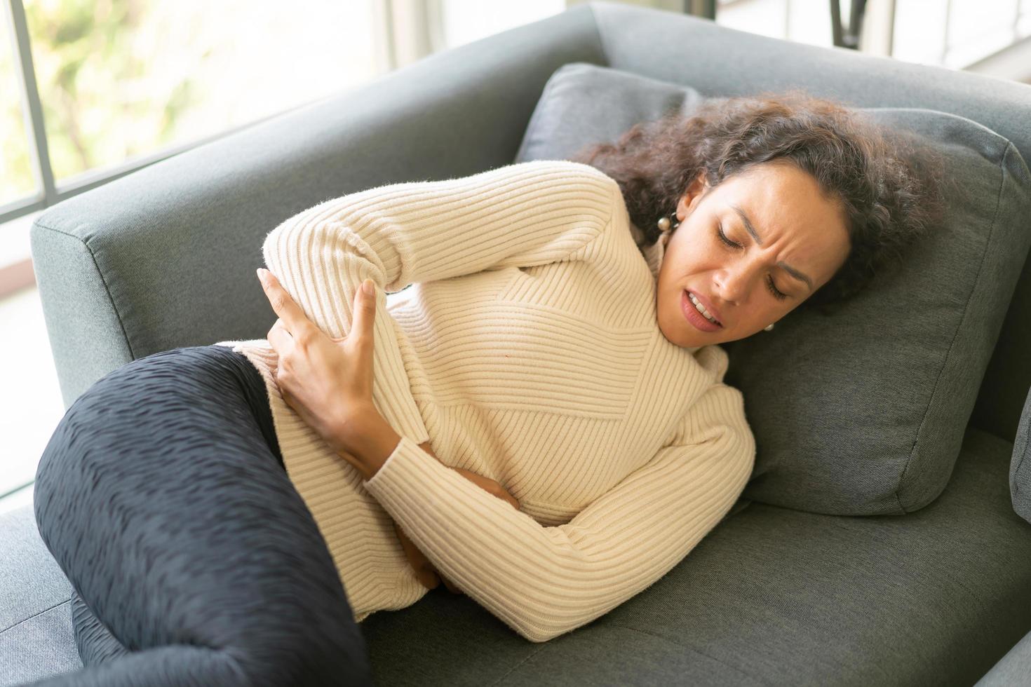 Latijnse vrouw liggend op de bank met buikpijn foto