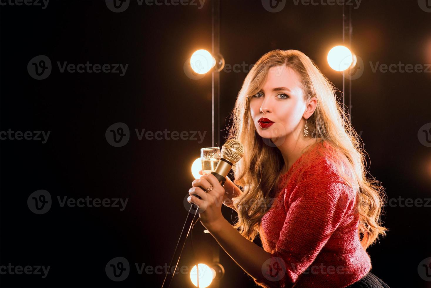 jonge smiley mooi lang haar in rode trui meisje met microfoon zingen lied op het podium in karaoke foto