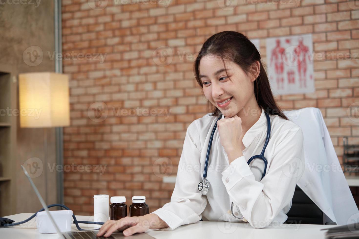 portret van mooie vrouwelijke arts van Aziatische etniciteit in wit overhemd met stethoscoop, glimlachend en kijkend naar de camera in de kliniek van het ziekenhuis. één persoon met expertise in professionele behandeling. foto