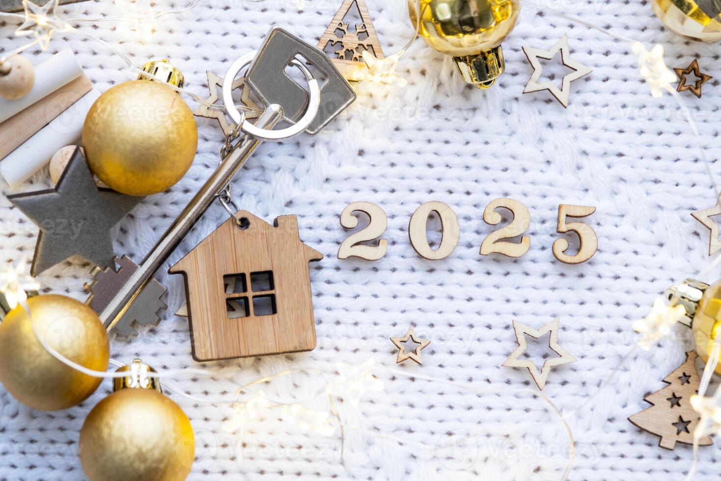 huis sleutel met sleutelhanger huisje Aan feestelijk achtergrond met sterren, lichten van slingers. nieuw jaar 2025 houten brieven, groet kaart. aankoop, bouw, verhuizing, hypotheek, verzekering foto