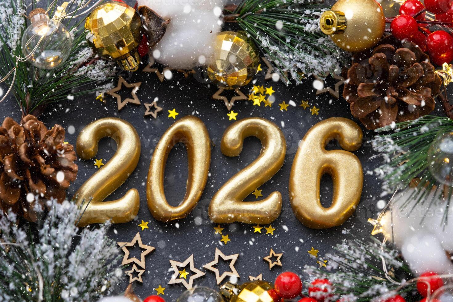 de gouden figuren 2026 gemaakt van kaarsen Aan een zwart steen leisteen achtergrond zijn versierd met een feestelijk decor van sterren, pailletten, Spar takken, ballen en slingers. groet kaart, gelukkig nieuw jaar. foto