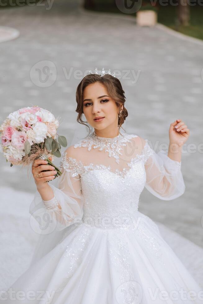 brunette bruid in off-the-schouder kant wit jurk en tiara poseren met een boeket van wit en roze bloemen. mooi haar- en verzinnen. voorjaar bruiloft foto