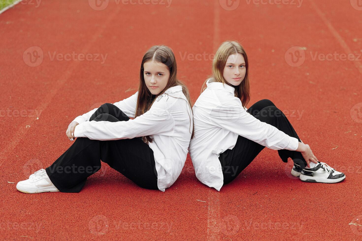 portret van twee tiener- meisjes in gewoontjes kleren zittend in een stadion en poseren op zoek Bij de camera. concept van vriendschap. een moment van geluk. foto