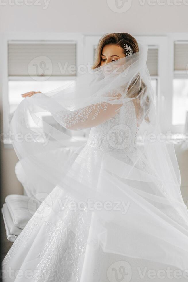 portret van een inschrijving bruid in een bruiloft jurk en een mooi kapsel onder een sluier in haar kamer van de ochtend- foto